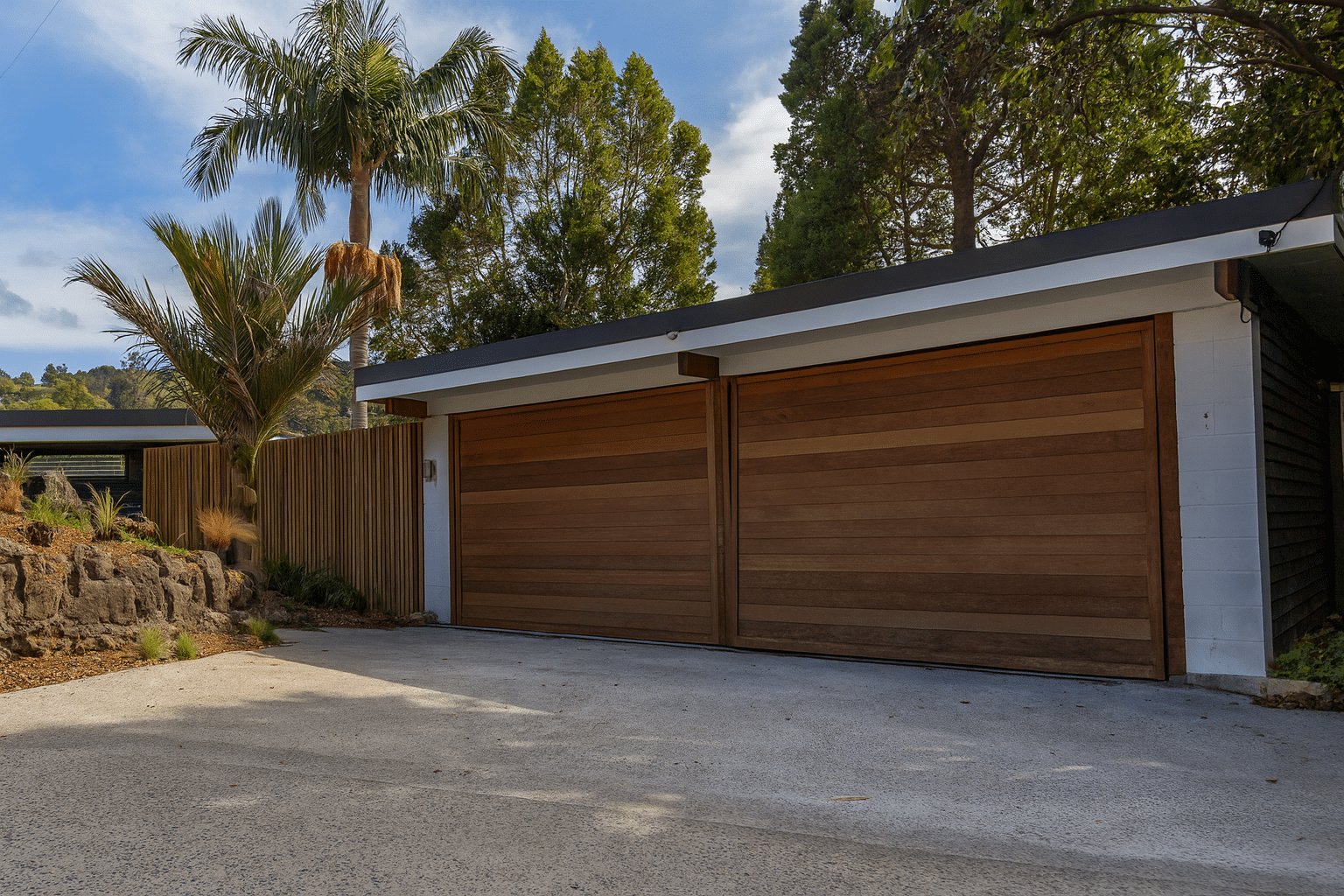 Modern double garage with wooden doors and concrete driveway surrounded by palm trees